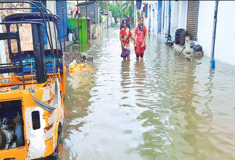 பள்ளிக்கரணை நாராயணபுரம் ஏரி நிரம்பியதால் வீடுகளை சுற்றிலும் தேங்கி நிற்கும் தண்ணீரில் நடந்து வரும் பெண்கள்