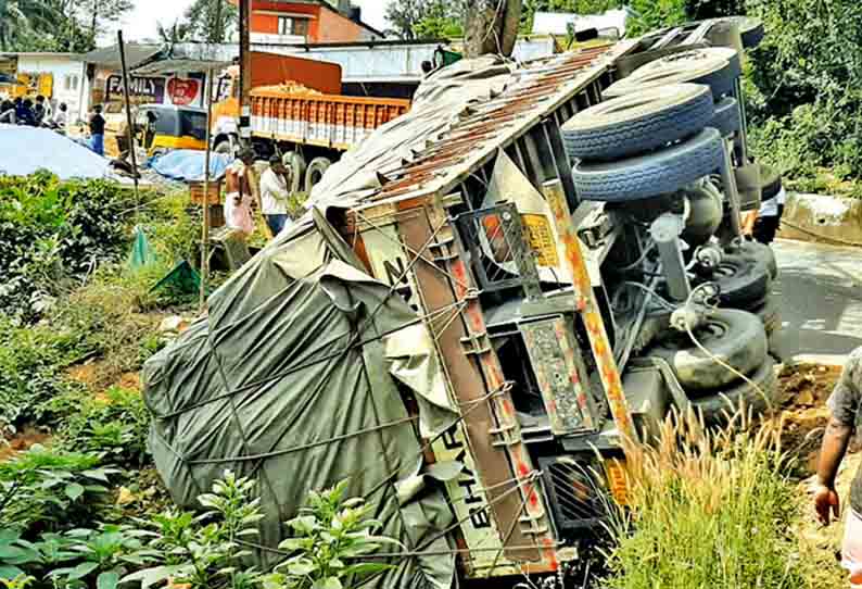 கூடலூரில், சாலையோர பள்ளத்தில் சரக்கு லாரி கவிழ்ந்தது - லேசான காயத்துடன் டிரைவர் உயிர் தப்பினார்