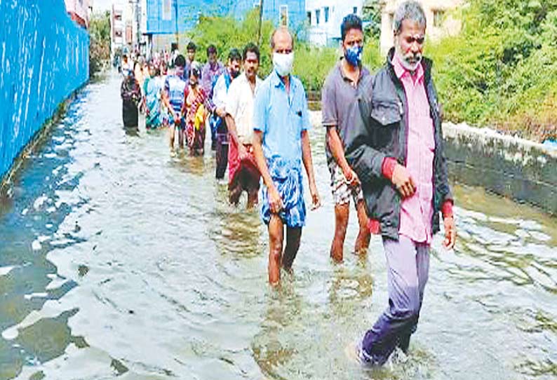 தேங்கிய மழை நீரில் நடந்து செல்லும் பொதுமக்கள்.